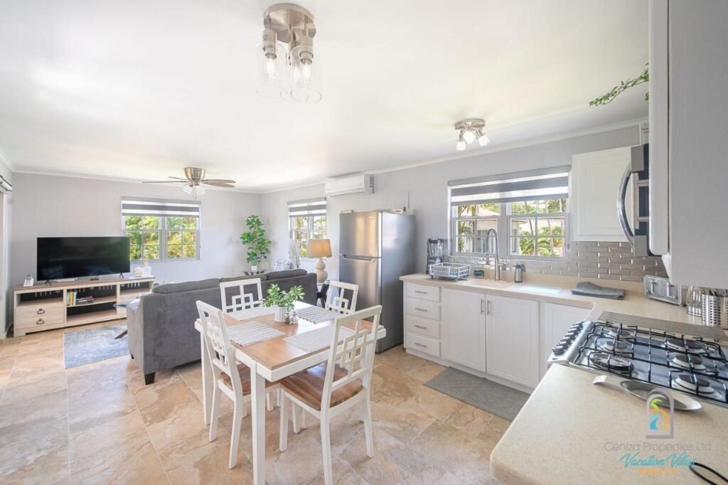 Sala de estar e cozinha do Dover Court Apartments - Steps to St Lawrence Gap. Uma cozinha e uma mesa do lado direito, do lado esquerdo a sala com TV.