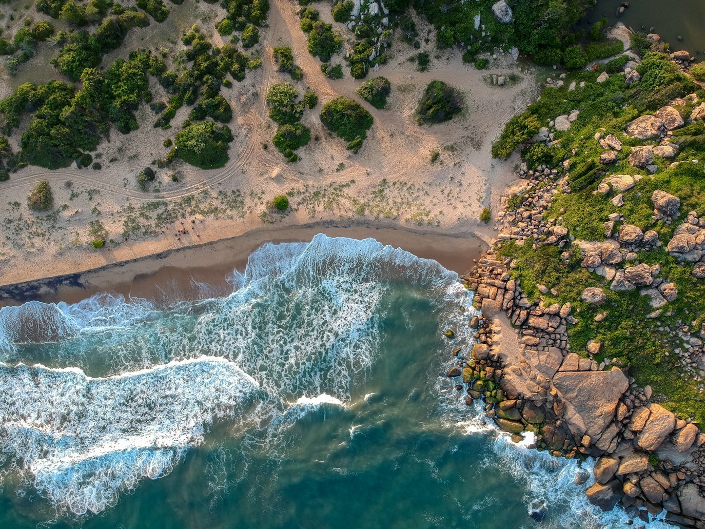 Vista aérea de um litoral de Lahugala com ondas batendo na praia de areia, cercada por vegetação verde e terreno rochoso à direita. Representa o que fazer no Sri Lanka.