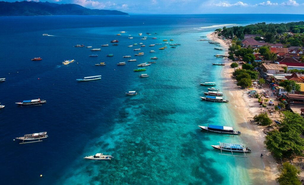 Gili Trawangan na Indonésia, onde a praia tem uma faixa pequena de areia, onde o mar é azul claro e há alguns barcos parados. Representa eSIM Indonésia.