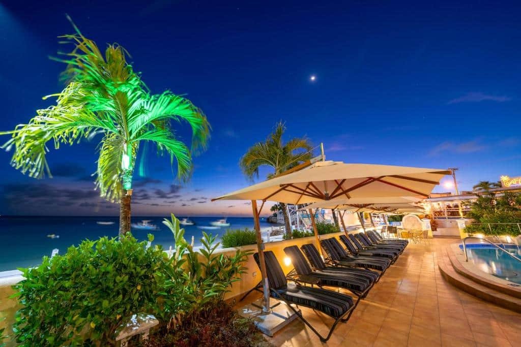 Área externa, com piscina, espreguiçadeiras e barcos no mar do Yellow Bird Hotel